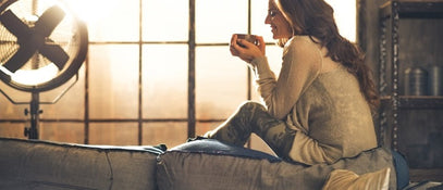 A woman sat holding a cup of tea next to a window
