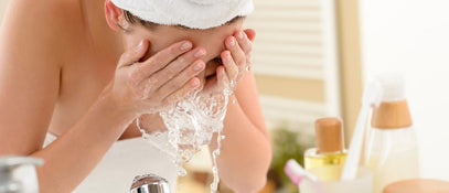 A woman wearing a turban leaning over a sink washing her face with splashing water