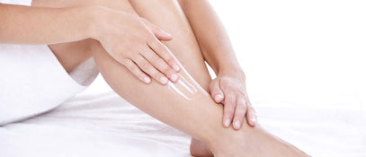 A close up of a woman rubbing cream onto her shin with her right hand