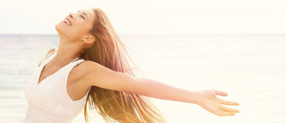 A women standing in front of the sea smiling with her arms outstretched